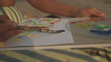 indian adult girl paints skilful brush strokes on paper on her lap, close up