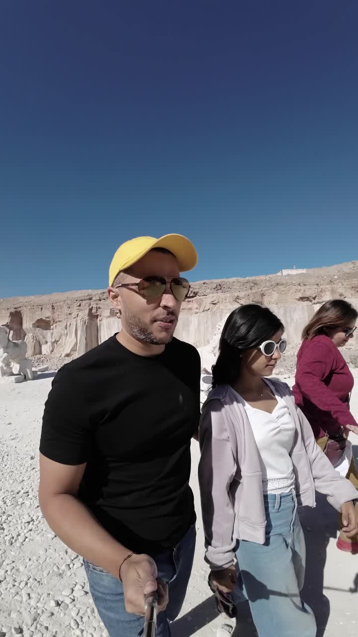 Un uomo e due donne che camminano in un paesaggio desertico roccioso con sculture.