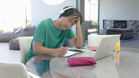 teenage asian boy studying on laptop at a modern home setting