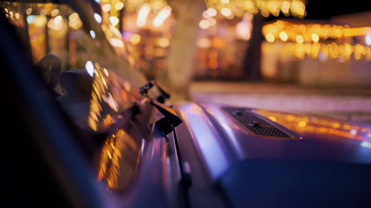 Close up of a vehicle hood reflecting warm golden city lights at night