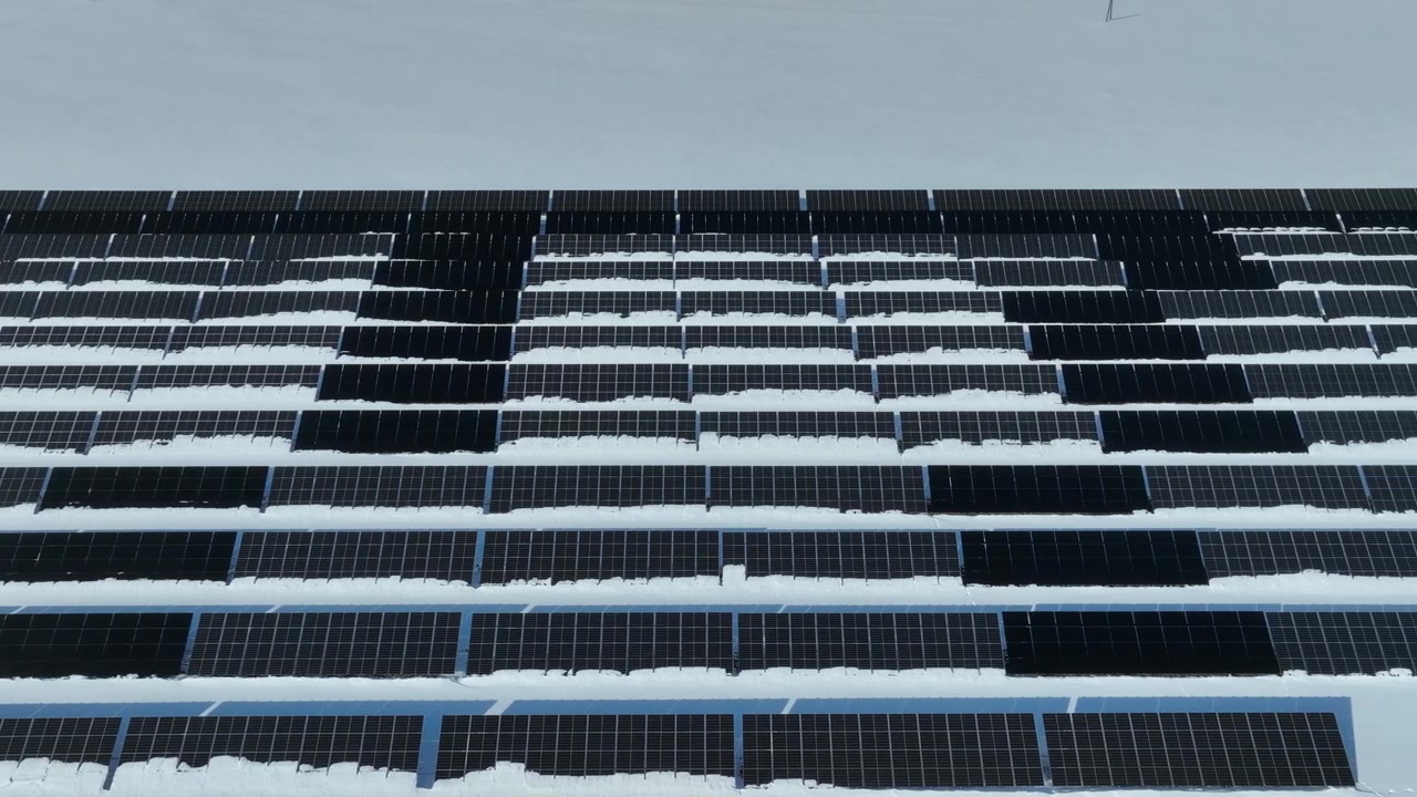 Dron letící bokem podél panelů solární elektrárny v řadě na zasněžených polích, Estonsko