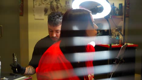 rack focus reveals tattoo artist carefully working with female client at the studio