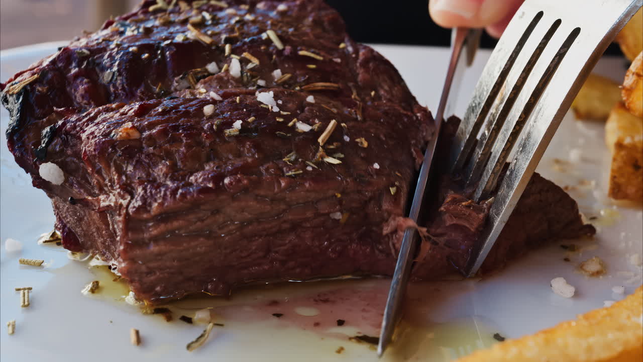 Close up of stake being cut near with fries and salad on a white plate