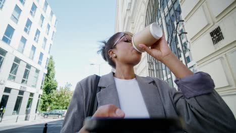 businesswoman texting while walking on a city street with coffee.