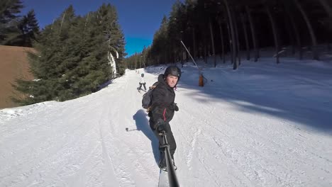 vista frontal de un snowboarder bajando la colina con selfie stick en un día despejado