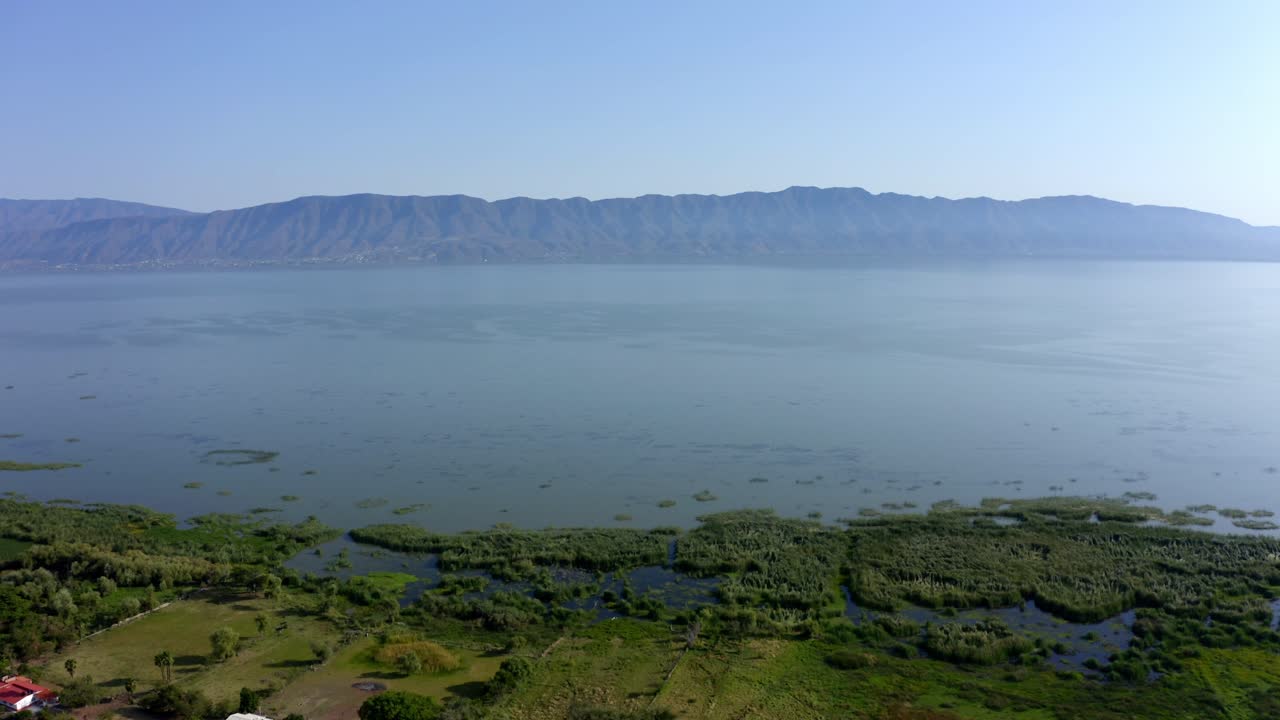 DRONE: DOLLY IN SHOT OF CHAPALA LAKE AT NOON WITH MOUNTAINS AT THE BACK