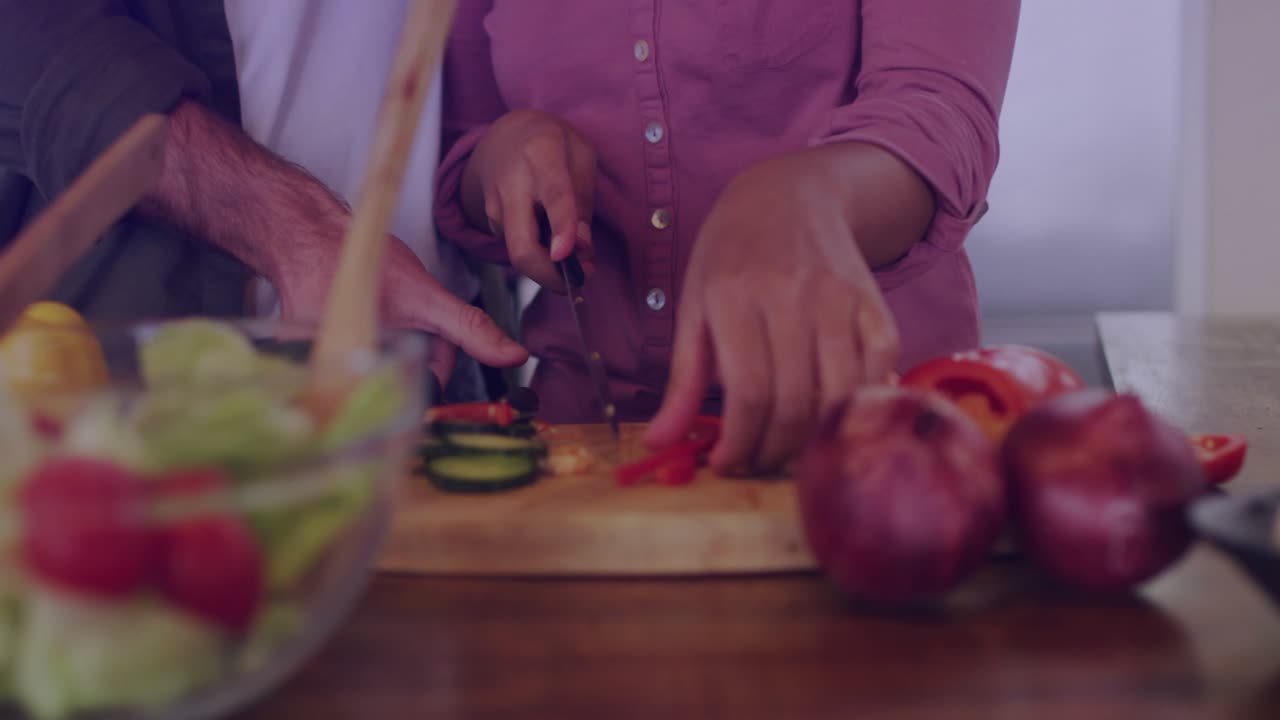 Female slicing cucumber initiating health HUD while partner steadying pepper before smiling at bowl