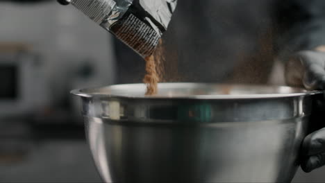 chef pouring chocolate powder into a metal bowl