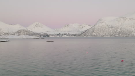 Aerial-view-over-fjord-of-snow-covered-mountains,-white-winter-landscape