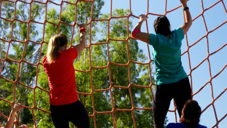 Female-trainer-assisting-women-in-climbing-net-during-obstacle-course