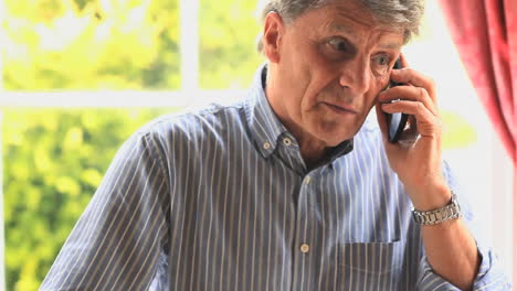 mature man sitting by a window talking on the phone