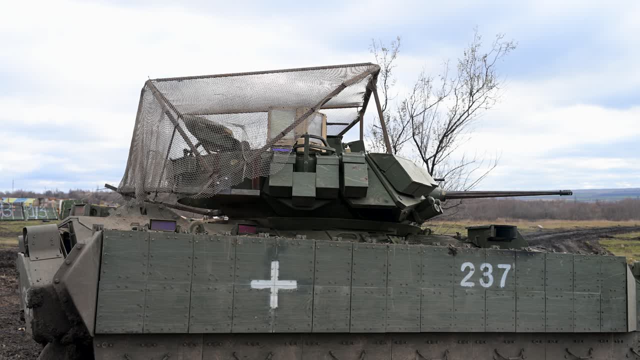 A shot of a US-made M2 Bradley IFV in Ukraine, a white medical cross, and an overhead 'cope cage' for protection against drones