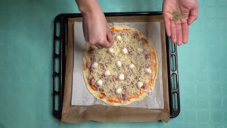 Luftaufnahme-Von-Händen-Mit-Oregano-Und-Einer-Frau,-Die-Zutat-Auf-Hausgemachte-Pizza-Legt