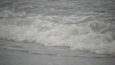 primer plano, la marea del océano chocando contra la orilla de la playa en un día sombrío en cámara lenta