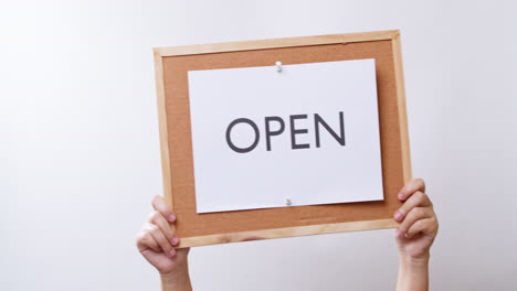 woman's hand shows the paper on board with the word open in white studio background with copy space