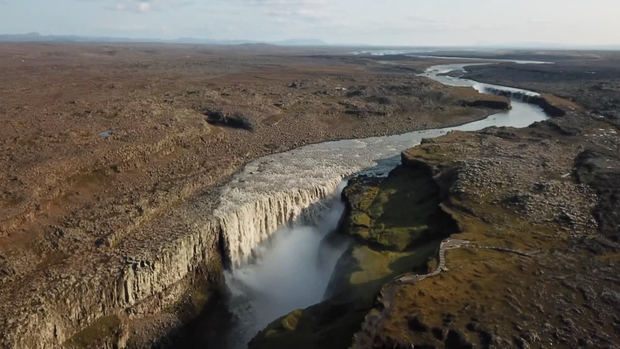 A breathtaking aerial view of Dettifoss, Iceland, highlighting the powerful waterfall cascading into rugged cliffs and surrounded by vast, barren landscapes under a serene sky