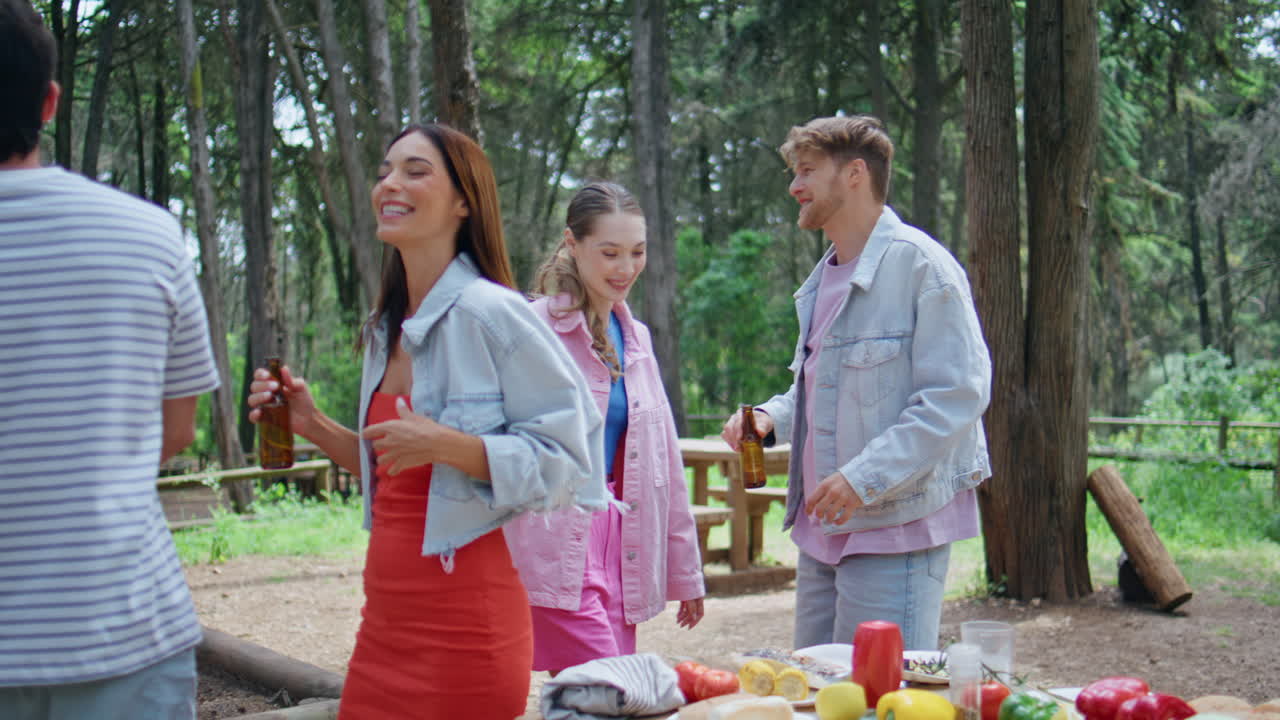 Dancing friends enjoying picnic in green park. Happy young people moving rhythm