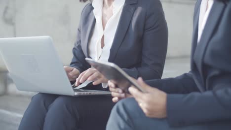 Friendly-Female-Colleagues-Sitting-Outside-And-Using-Laptop