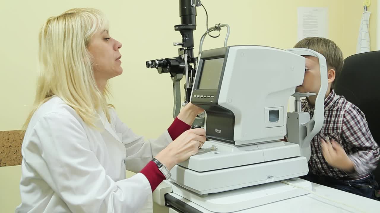 Side view of female pediatric optometrist examining eyes of little boy. Children ophthalmology
