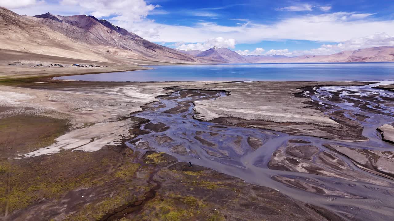 Melting icy water creating abstract curvy stream as it meanders over glacial flat stony lands to mountain lake. Drone fly over