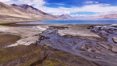 melting icy water creating abstract curvy stream as it meanders over glacial flat stony lands to mountain lake. drone fly over