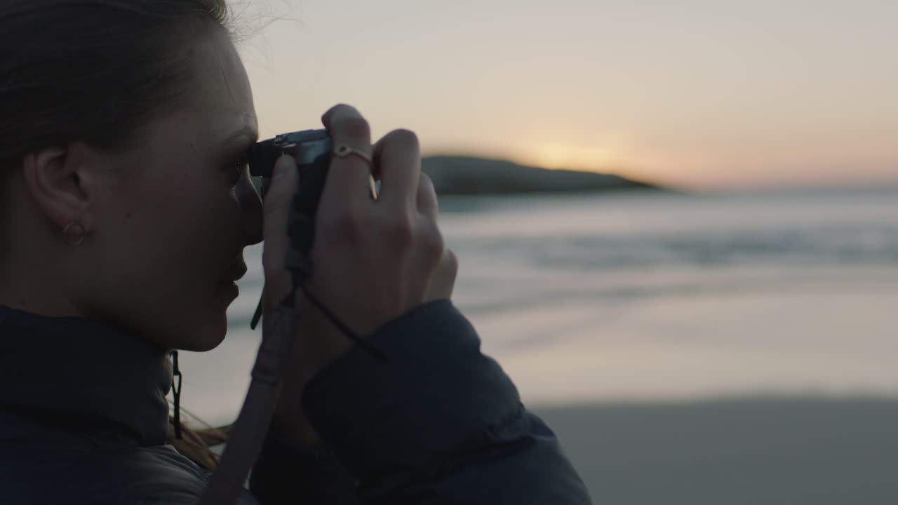 close up of young woman photographer on beach taking photo of seaside ocean at sunset using camera