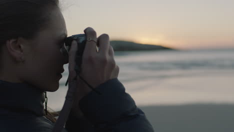 primer plano de una joven fotógrafa en la playa tomando una foto del océano costero al atardecer usando una cámara