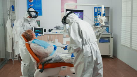 dentist in protective equipment reviewing x-ray using tablet