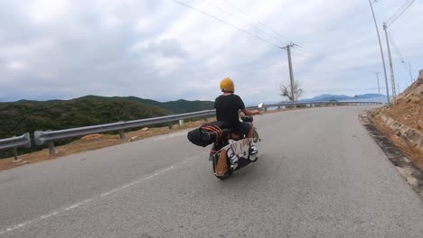 Vista-Trasera-De-Un-Motociclista-Que-Viaja-En-Una-Carretera-Costera-Con-Una-Tabla-De-Kitesurf-Atada-A-Una-Motocicleta