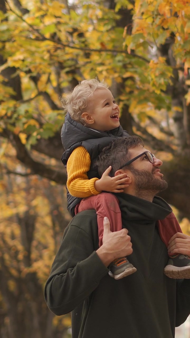 Padre che porta il figlio piccolo sulle spalle in un parco autunnale