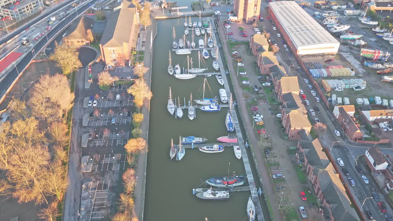 Aerial over Hull Marina entrance basin, lined with yachts and motorboats, flanked by brick dockside townhouses near the A63 in Kingston upon Hull, England