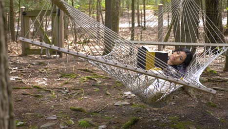 carefree young caribbean woman reading novel swinging in woodland hammock