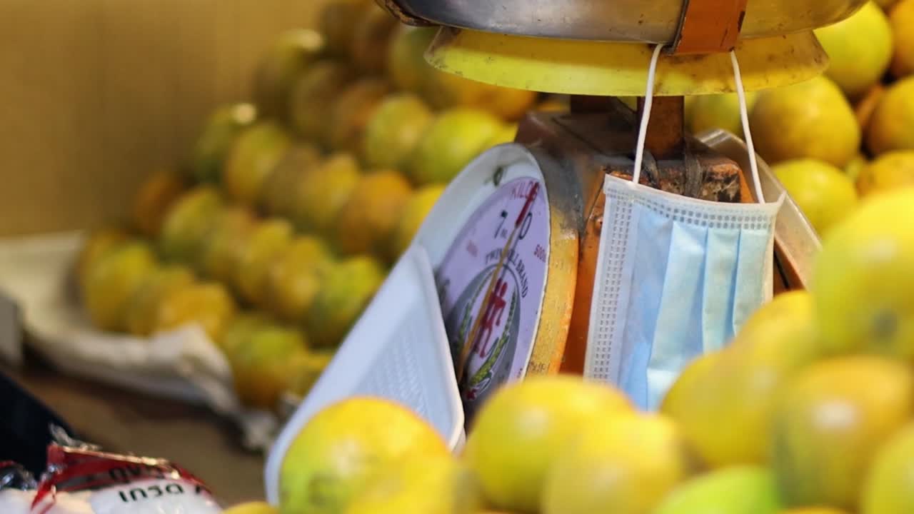 A person picks oranges from a pile, placing them into a plastic bag near a weighing scale.