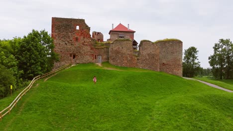 historic bauska castle towers over green hill as woman walks below in latvia