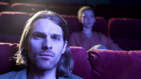 Close-Up-View-Of-Blond-Man-Sitting-In-The-Cinema-And-Looking-At-Camera-With-The-Lights-Off