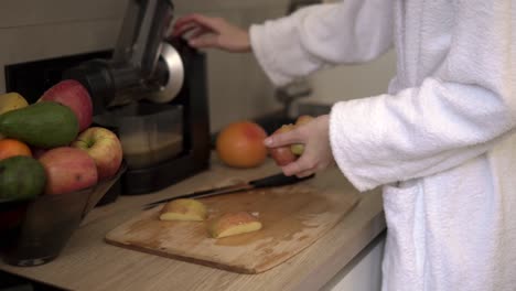 Unerkennbare-Frau-In-Weißem-Gewand,-Die-Morgens-Mit-Einem-Entsafter-Apfel--Oder-Birnensaft-Zubereitet