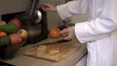unrecognizable woman in white robe making apple or pear juice in the morning using juicer