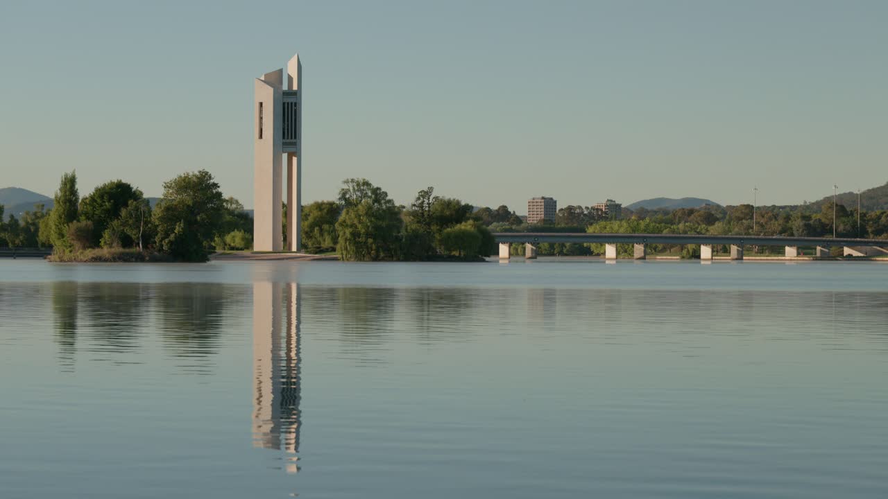 The National Carillon stands tall as the lake reflects its image like a mirror. The calm morning air and soft light create a breathtaking and serene moment in Canberra.