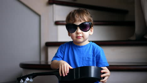beautiful baby boy wearing mom's sunglasses sits holding a guitar. toddler having fun at home.