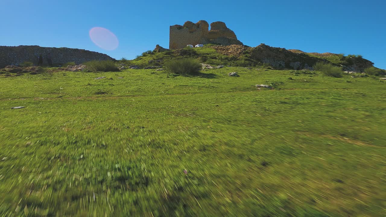 Ruins of the Castillo de la Pe&ntilde;a shrink as a drone flies backwards down a green, rocky hill in Andalusia, Spain