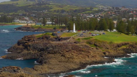 vehicles park beside the kiama lighthouse with townscape on the background