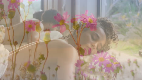 animation of pink flowers in garden over biracial woman lying on massage table