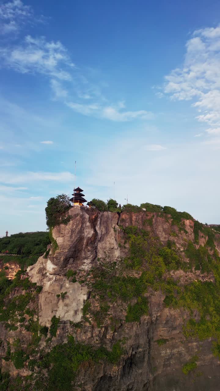 Vista verticale da drone che mostra l'iconica costa di Uluwatu, con le sue scogliere a picco, l'elevato tempio balinese e gli strati di roccia calcarea evidenziati sullo sfondo di un vivace scenario costiero e acque aperte