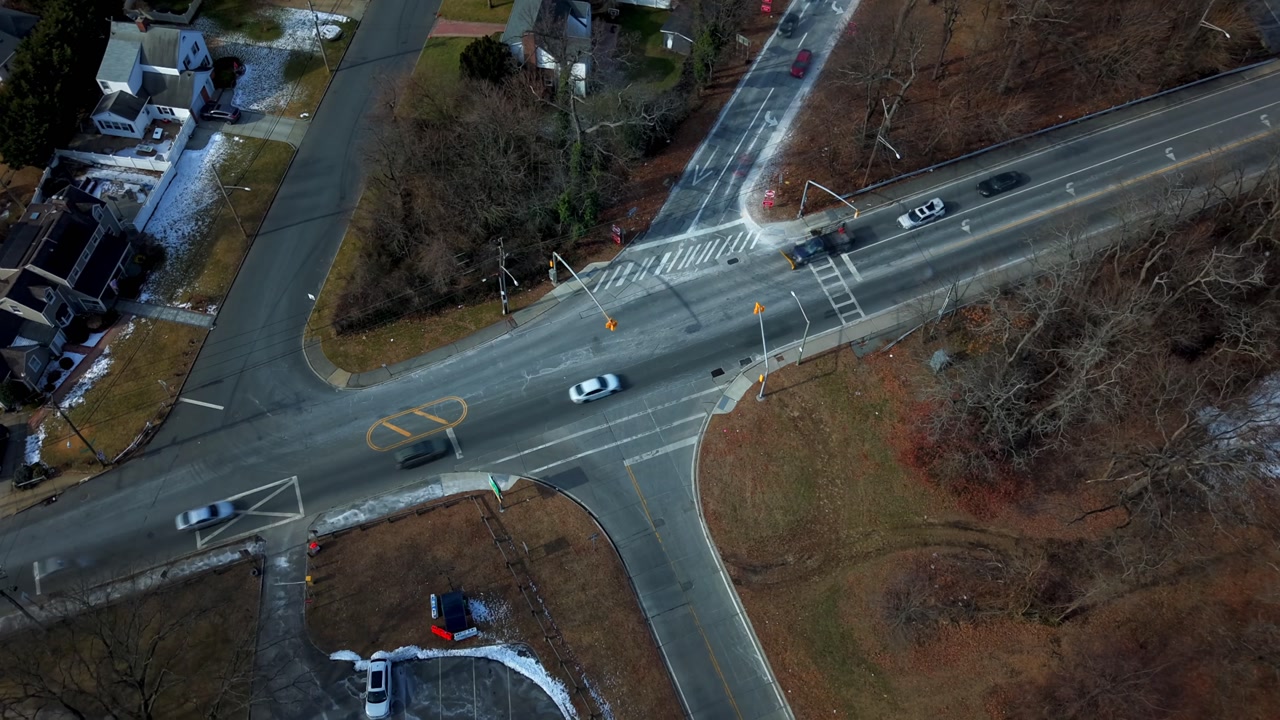 An aerial hyper lapse over a five way intersection on Long Island, on a sunny day in winter. The camera tilted downward, truck right orbiting the roads.