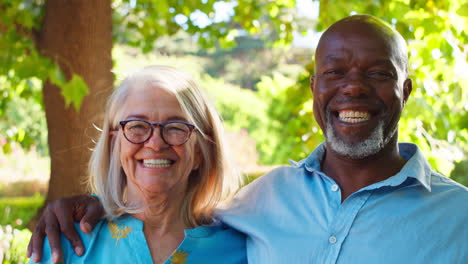 portrait of multi-racial senior couple standing outdoors in garden park or countryside