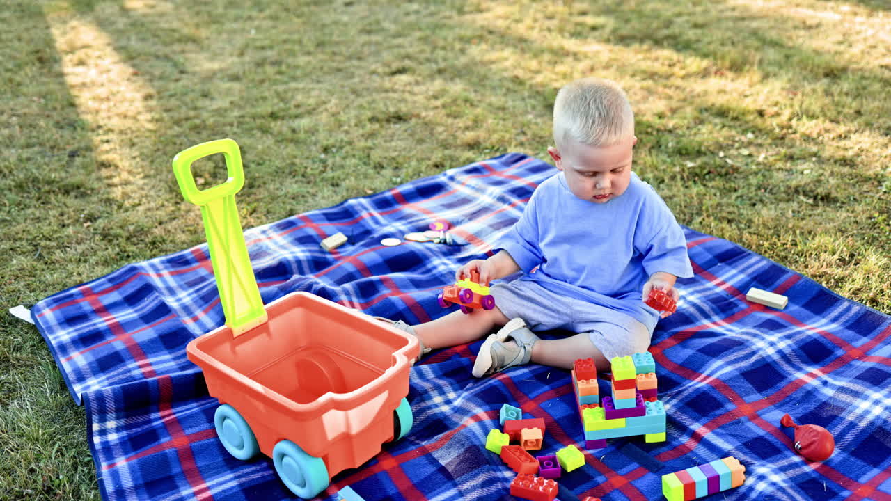 A little boy in a T-shirt and shorts sits on the grass outside and plays with a construction set. A child plays on a swing on a warm sunny day. Child development