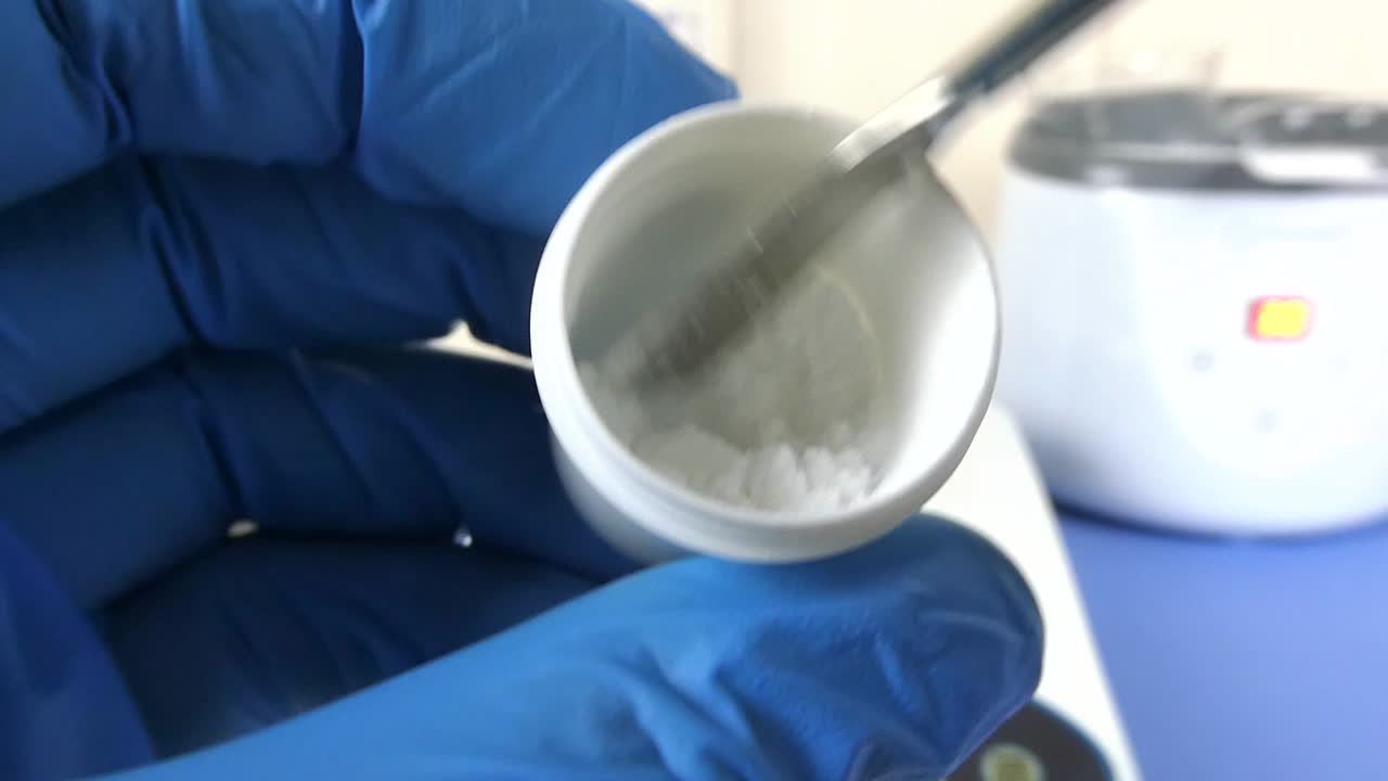Close-up of a laboratory technician's gloved hands performing a quality control test on hyaluronic acid powder in a cosmetic laboratory.