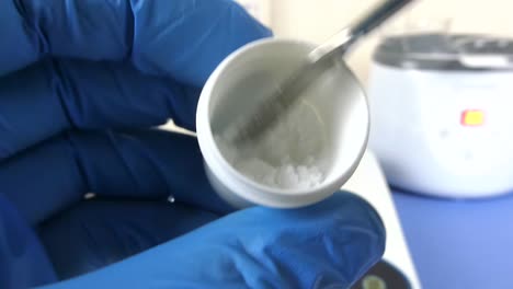 close-up of a laboratory technician's gloved hands performing a quality control test on hyaluronic acid powder in a cosmetic laboratory.