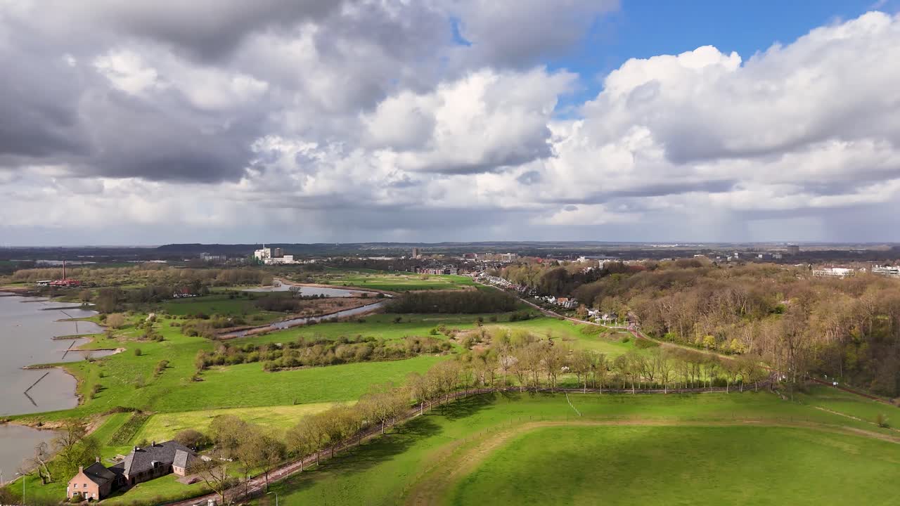 Veduta aerea di campi verdi, fiume e città lontana sotto un cielo nuvoloso