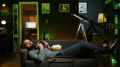 gamer lounged on couch playing videogames on console with bowl of popcorn in lap